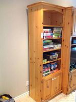 Solid pine wood shelving unit against wall holding various board games on shelves. Bottom section has two doors with white knobs.