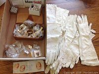 Wide shot showing assortment of lapel pins in plastic bags and leather trays alongside several pairs of white ladies leather gloves spread out.