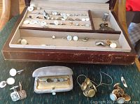 Full view of assortment of antique men's formal accessories shown in vintage display trays on green surface