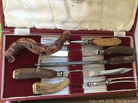 Carving set utensils arranged inside an open red velvet lined box with cream satin lid.