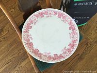 16 inch round Wedgwood cake plate with pink floral border on white, shown face up on a chair