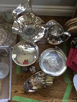Top view showing an arrangement of vintage silver plate items including pedestal tray with pierced design, water jug, lidded vessel, salt and pepper shakers, sugar scoop and ladle, small bowls and vase.