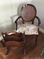 Photo showing wood chair with cane back and floral upholstered seat with vintage wood magazine rack in front