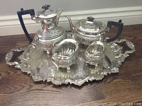Full view of the silver plated tea and coffee service set on a wooden floor including tray, coffee pot, teapot, creamer, and sugar bowl