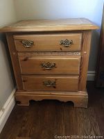 Front view of nightstand showing three closed drawers and brass-finish drop bail handles