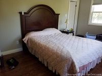 Full queen bed made of dark polished wood with light pink coverlet and white bed skirt in bedroom setting.
