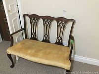 Front view of antique wooden love seat with upholstered golden seat showing wear and stains.
