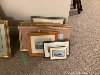 View of 8 framed prints stacked on floor showing variety of frames sizes and colors