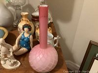 Pink satin glass vase, oil lamp with two hurricane shades, figurines, and various vases visible on wooden surface