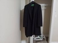 Mens single breasted dark wool and cashmere coat hanging on hanger against white wall.