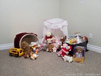 Photo showing largest view of the children's toys lot including white doll crib with canopy, pink doll bed, basket with red liner, various stuffed animals and toy bus scattered on carpeted floor.