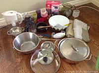Full lot overview showing pots, bowls, colander, utensils, and fabric items on hardwood floor