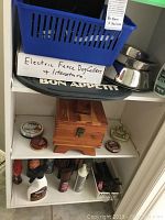 Shelving with blue basket labeled electric fence dog collars and literature, metal dog bowls, wooden shoe shine kit box, and tins of shoe polish and other treatments.