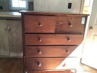 Full front view of vintage wooden high boy dresser showing five drawers with round knobs, clean medium brown wood finish with some marks and paint splattered spots, overall sturdy structure.