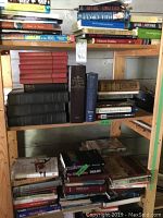 Three shelves filled with hardcover and softcover books on a wooden shelving unit, featuring titles related to history, literature and fiction.