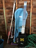Photo showing blue Rossignol cross country skis standing in a blue plastic toboggan sled with ski poles, bags, and some additional sports equipment scattered around.