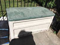 Full view of the Suncast deck box showing beige plastic base and sun faded green lid, exterior shows dirt and scratches.