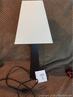 Full view of table lamp showing black base and white shade with attached cord.
