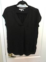 Black V-neck blouse hanging on a black hanger against a white door.