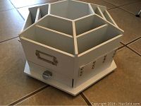 Full view of the white wooden hexagonal lazy Susan style craft organizer showing six divided slots and metal hooks on the sides.