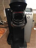 Front top view showing open K-Cup compartment and sharp needle piercing chamber inside the Keurig coffee maker.