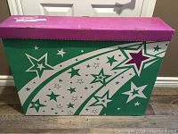 Sealed bulletin board box with star design and purple lid on floor near door
