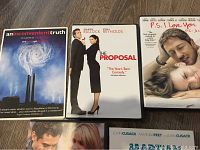 6 DVD cases shown on wooden floor. Titles: An Inconvenient Truth, The Proposal, P.S. I Love You, The Holiday, Martian Child, and partially visible sixth DVD.