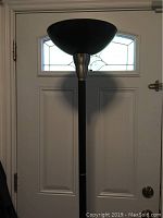 Full view of the black and silver floor lamp showing the bowl-shaped top shade and black pole against a white door