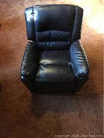Front view of a child sized black leather reclining chair with padded armrests and backrest on brown carpet.
