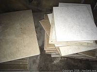 Stack of large square ceramic floor tiles in beige and cream shades on concrete floor