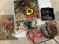 Top-down view of multiple boxes and trays filled with various costume jewelry including bracelets, rings, watches, and necklaces in different colors and materials.