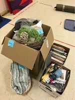 Wide shot of large box filled with yarn skeins and knitting projects, next to boxes containing books and needlecraft items