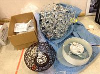 Full view of chandelier with glass leafy design, and two ceiling light fixtures with metal and plastic/glass construction, shown with packing material and cardboard box