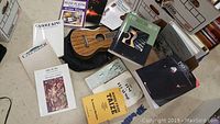 Overview of the ukulele placed on the floor surrounded by several music songbooks and the instruction book.