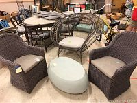 Photo showing two grey resin wicker-style chairs with beige cushions and a handmade oval cement table positioned between them.