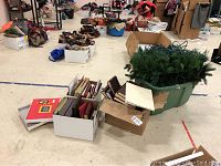 Photo showing a green faux Christmas wreath in a plastic container beside boxes and stacks of photo albums on the floor.