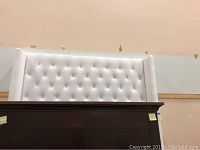 Front view of the tufted white velveteen queen headboard against a beige wall.