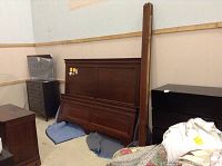 The full set of bed frame components leaning against the wall on a padded blanket, showing the deep wood finish and rectangular paneled design of the headboard and footboard.