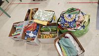 Seven boxes of assorted kitchen and dining linens including tablecloths and napkins, visible fabrics of varied colors and patterns.