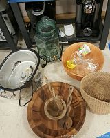 Photo of lot items on floor showing coffee makers, beverage dispenser, wooden bowls with wooden utensils, woven basket, and mugs.