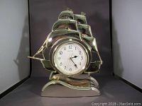 Front view showing polished brass sailing ship clock with circular white clock face and moving sails design.