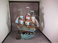 Front and side view of a vintage-style wind-up tin sailboat music box on wave-shaped blue base