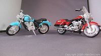 Side view of blue Honda Shadow American Classic model and red Harley Davidson Road King model motorcycles on gray surface under soft lighting.