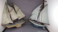 Front view showing two metal sailboat wall hangings side by side, highlighting the different hull colors and the detailed sail structures.