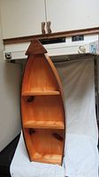 Front view of wooden boat-shaped shelf showing three shelves inside