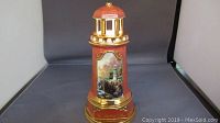 Front angle of the lighthouse figurine showing the painted lighthouse image and gold-tone base.
