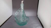 Front view of clear glass ship-shaped oil lamp with wick.