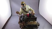 Front view of pirate figurine sitting on a treasure chest filled with gold coins and jewelry, showing detailed pirate clothing and accessories.