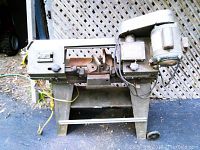 Full view of the older metal cutting band saw showing the vise and motor placement on a metal frame.
