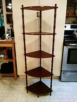 Front view of the wooden corner curio shelf showing five triangular shelves and turned vertical posts with finials.